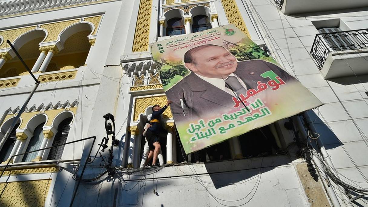 Des Algériens décrochant le portrait d'Abdelaziz Bouteflika de la façade du siège du Rassemblement national démocratique (RND) du Premier ministre Ahmed Ouyahia, à Alger, le 22 février 2019.
