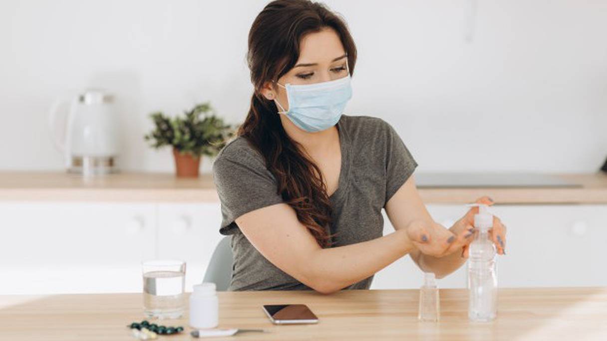 Une femme utilise du gel hydro-alcoolique et porte un masque sanitaire, deux gestes barrières de protection contre le coronavirus. 
