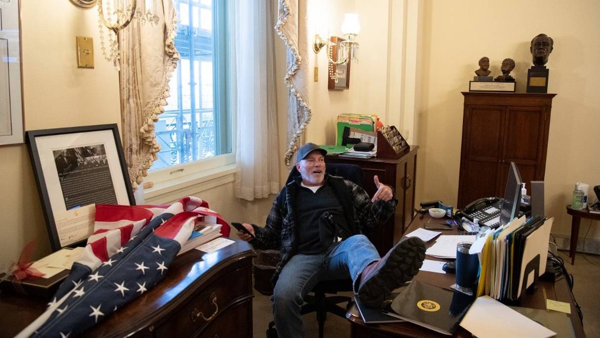Un supporter de Donald Trump, Richard Barnett, est assis sur le siège de Nancy Pelosi, présidente de la Chambre des représentants américaine, un pied posé sur son bureau, lors de l'assaut de pro-Trump contre le Capitole, le 6 janvier 2021, à Washington DC. 
