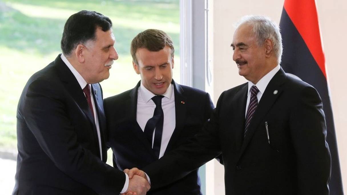 Le Premier ministre libyen Fayez al-Sarraj (g) et le général Khalifa Haftar, chef d'une force baptisée Armée nationale libyenne (ANL), se serrent la main devant le président français Emmanuel Macron, à la Celle-Saint-Cloud, près de Paris, le 25 juillet 2017.
