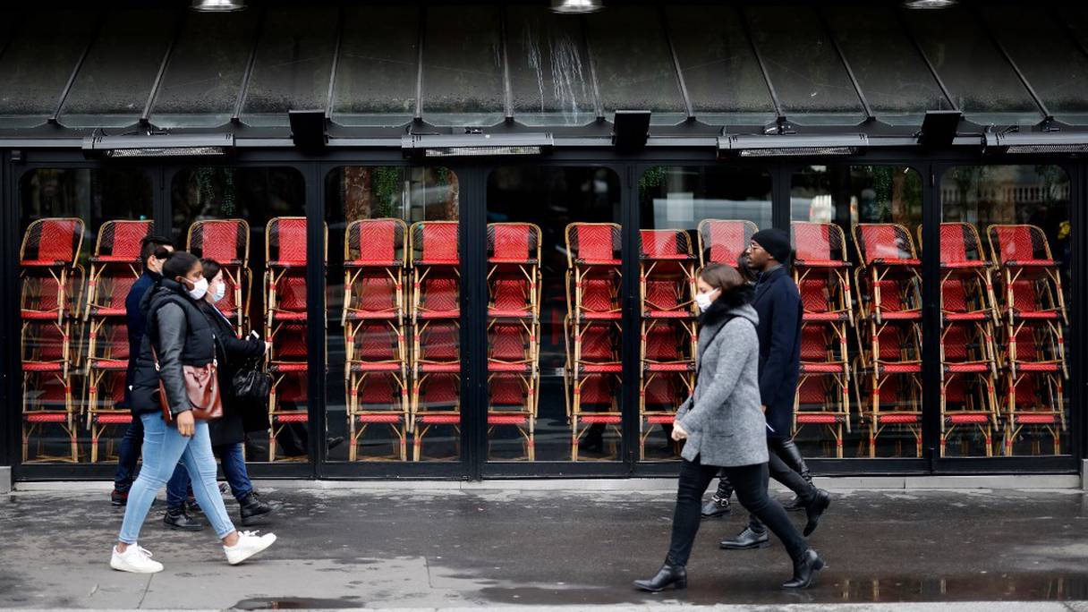 Des passants portant des masques de protection marchent devant un restaurant fermé, l'une des mesures de restriction qui doit endiguer la propagation du coronavirus, à Paris, le 23 novembre 2020. 
