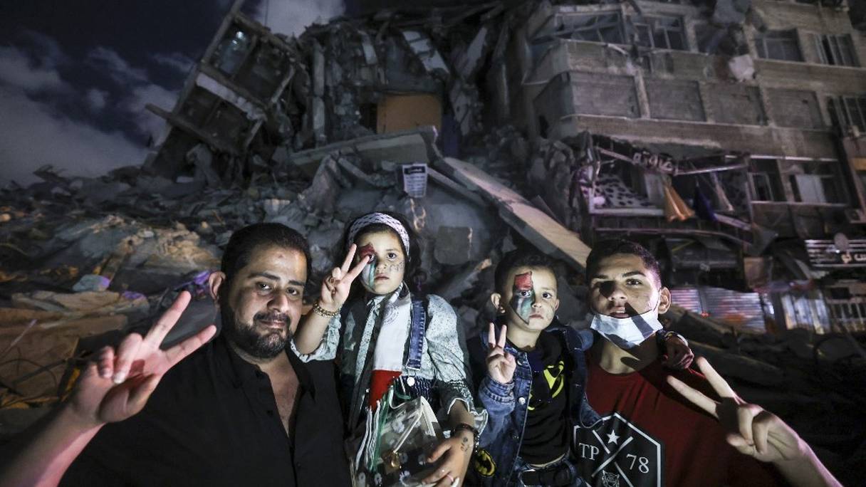 Un Palestinien pose pour une photo avec ses enfants devant le bâtiment détruit Al-Shuruq, détruit par une frappe aérienne israélienne, le 21 mai 2021, dans la ville de Gaza. 
