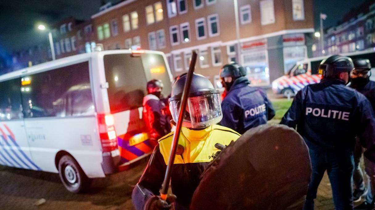 Un policier casqué et protégé d'un bouclier anti-émeutes tient une matraque, près d'un fourgon de police sur Beijerlandselaan, à Rotterdam, le 25 janvier 2021. 
