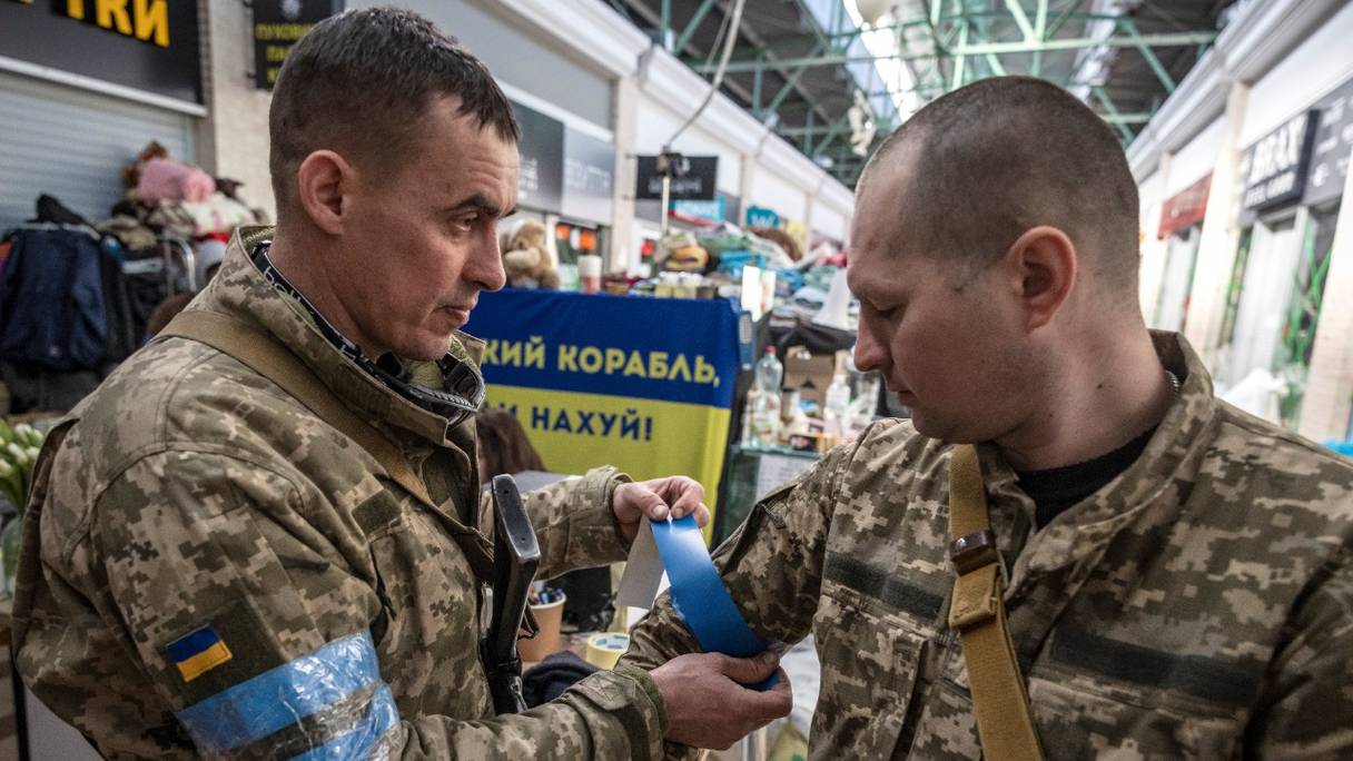 Des soldats ukrainiens mettent du ruban adhésif bleu sur leur uniforme, à Kiev, le 21 mars 2022.
