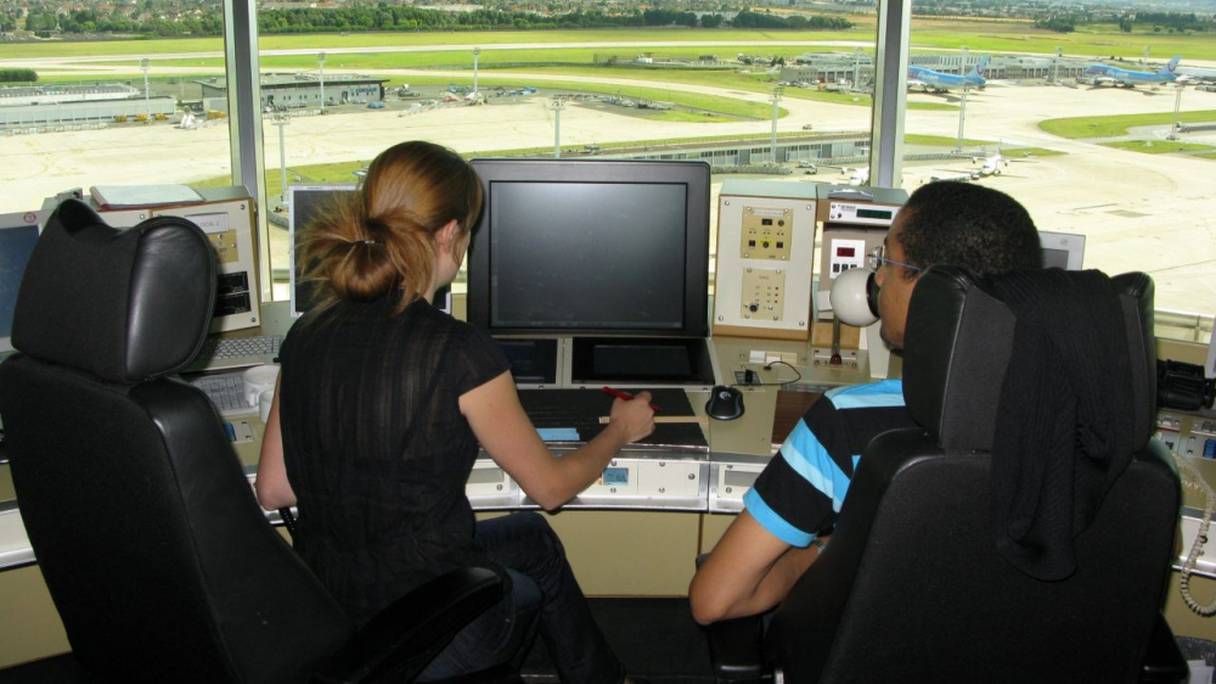 Des contrôleurs aériens, face à leur écran, au poste de commande de la tour de contrôle d'un aéroport. 
