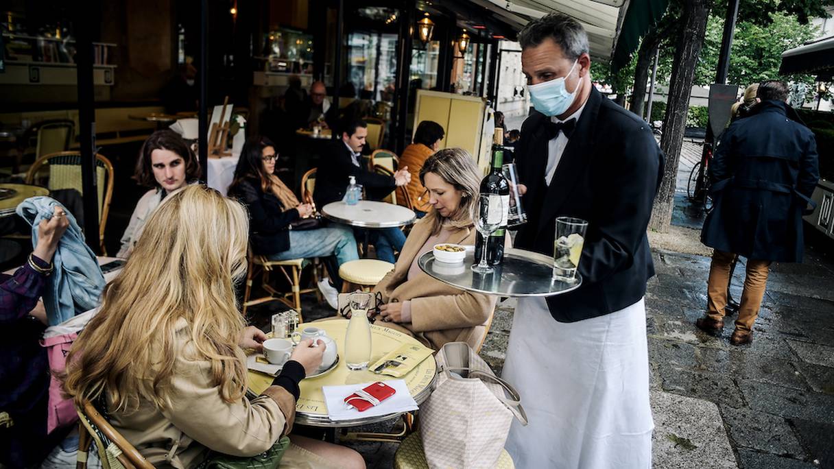 Un serveur sert des clients à la terrasse du café emblématique "Les Deux Magots", à Paris, le 19 mai 2021. 
