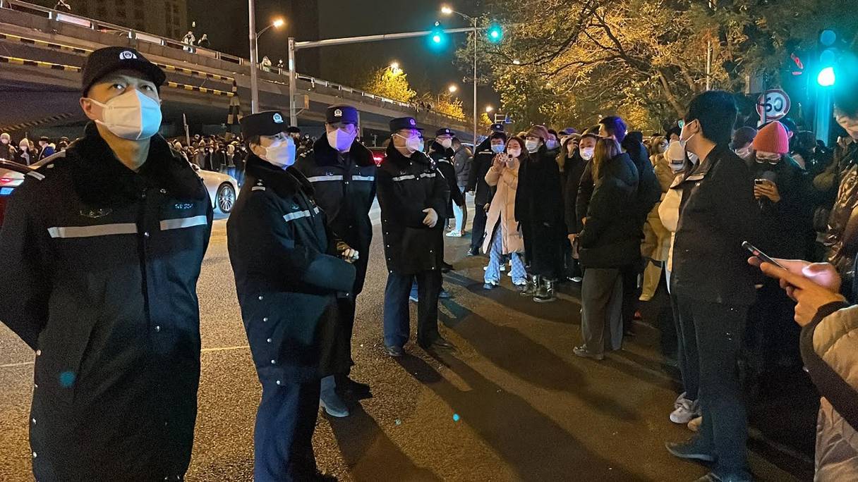 Des policiers surveillent des manifestants qui se rassemblent le long d'une rue, dans le contexte d'une série de manifestations contre les dures restrictions imposées par la Chine sur le Covid-19, à Pékin, le 28 novembre 2022.
