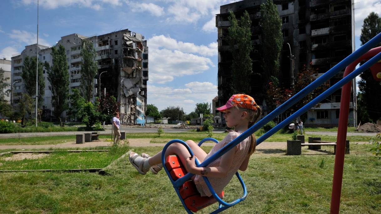 Une petite fille joue à la balançoire dans une aire de jeux devant un immeuble résidentiel détruit de la ville de Borodyanka, le 7 juin 2022, au cours de l'invasion russe de l'Ukraine.
