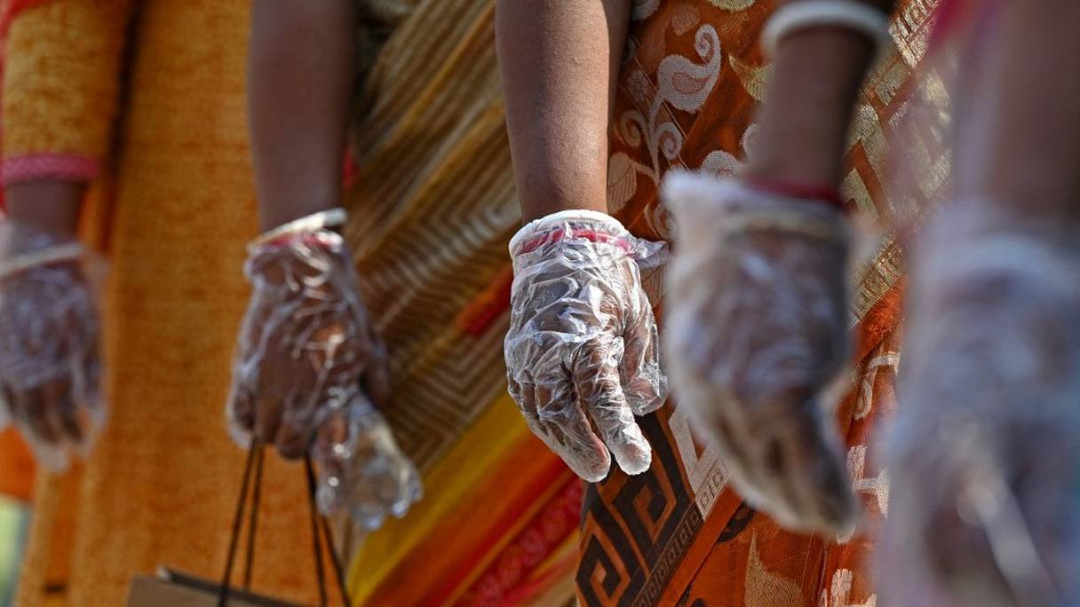 Des électeurs portent des gants, suivant les protocoles du coronavirus Covid-19, et font la queue dans un bureau de vote pour voter lors de la cinquième phase des élections à l'Assemblée législative de l'Etat du Bengale occidental, à Calcutta, en Inde, le 17 avril 2021.
