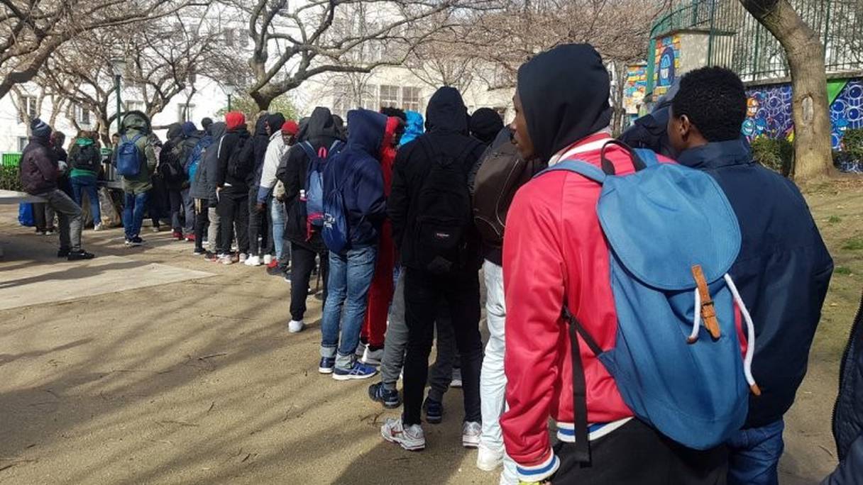 De jeunes migrants font la queue pour recevoir un repas chaud au jardin de la rue Pali-Kao à Paris. 
