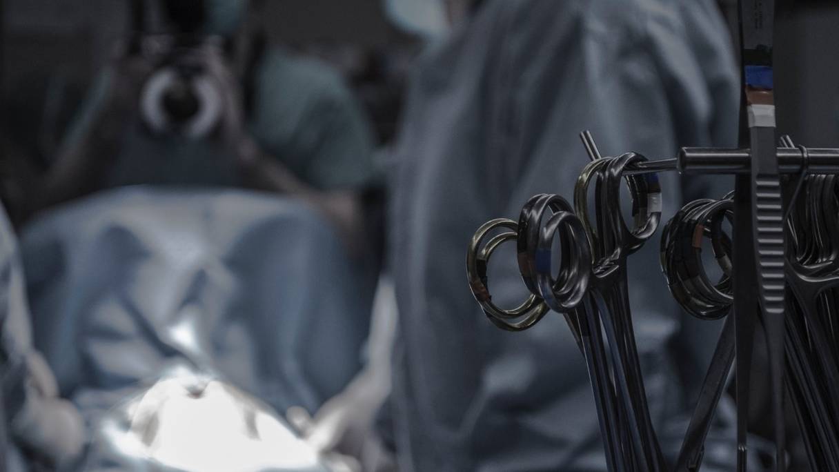 Instruments chirurgicaux, dans un bloc opératoire, alors qu'une équipe médicale est à l'œuvre. 
