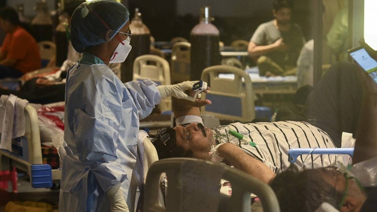 Un agent de santé portant un équipement de protection individuelle utilise un oxymètre et vérifie la saturation en oxygène dans le sang d'un patient atteint du Covid-19, à l'intérieur d'une salle de banquet convertie en centre de soins à New Delhi, le 7 mai 2021.
