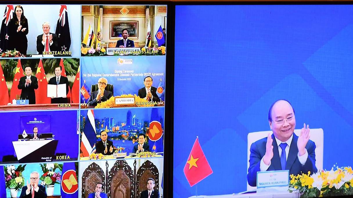 Le Premier ministre vietnamien Nguyen Xuan Phuc (à droite), photographié sur un écran aux côtés d'autres dirigeants parties prenantes à cet accord, applaudit lors de la cérémonie de signature virtuelle, depuis Hanoï, le 15 novembre 2020. 

