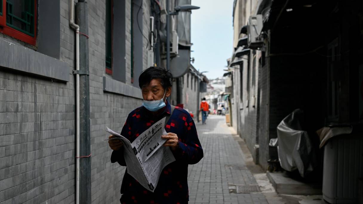 Un homme âgé lit un journal en marchant dans une ruelle de Pékin, le 9 mai 2022.
