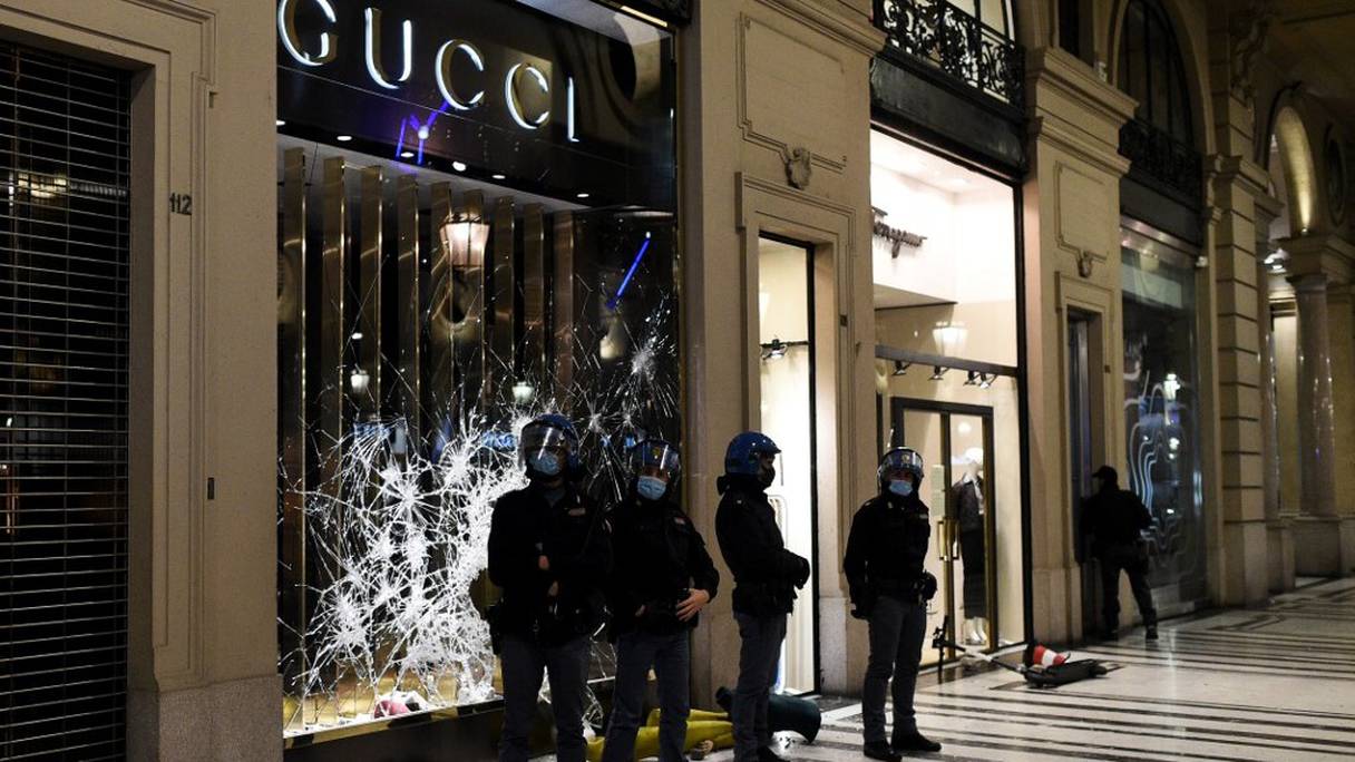 Des officiers de la police italienne se tiennent devant un magasin vandalisé après des manifestations de protestation contre les nouvelles mesures restrictives édictées par le gouvernement pour infléchir la courbe des contaminations. Centre-ville de Turin, le 26 octobre 2020. 
