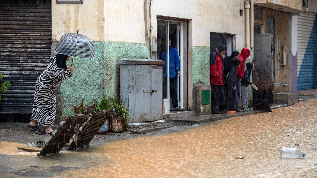 Des personnes s'abritent de la pluie dans une rue inondée par temps orageux à Fnideq, dans le nord du Maroc, le 5 mars 2021.

