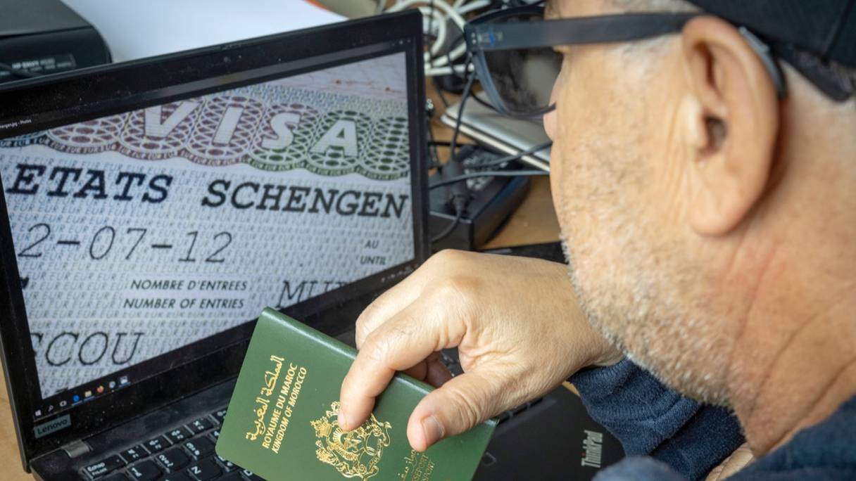 Un Marocain tient son passeport devant son ordinateur affichant un visa Schengen dans la capitale Rabat, le 28 septembre 2021.
