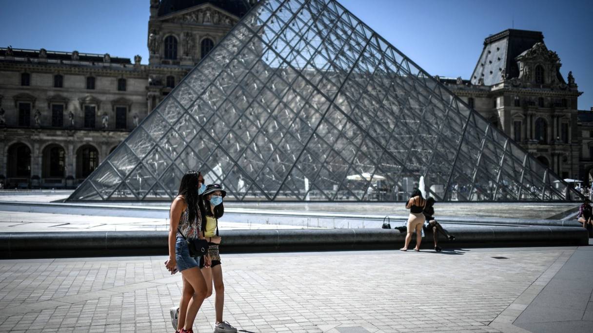 Personnes portant un masque sanitaire, devant la pyramide du Louvre, au milieu de la cour Napoléon du musée du Louvre, à Paris.
