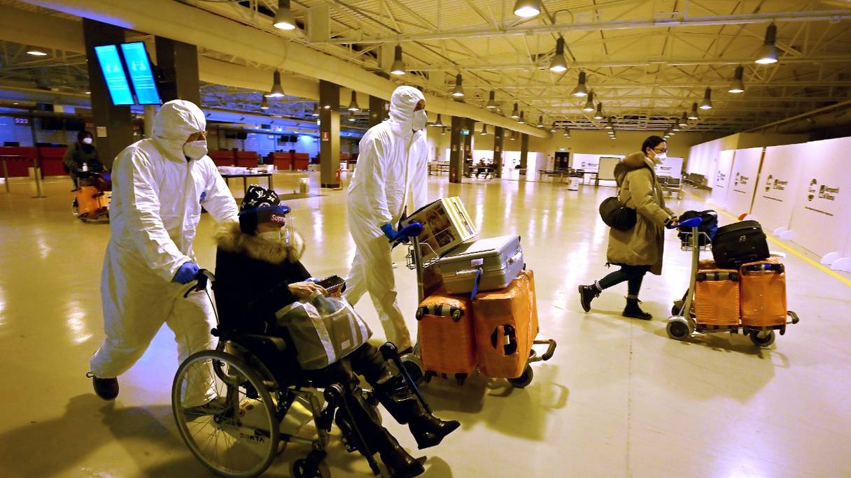 Des travailleurs portant des combinaisons de protection aident les voyageurs chinois à quitter le hall d'arrivée de l'aéroport de Rome-Fiumicino, le 29 décembre 2022 après avoir été testés pour le coronavirus Covid-19.
