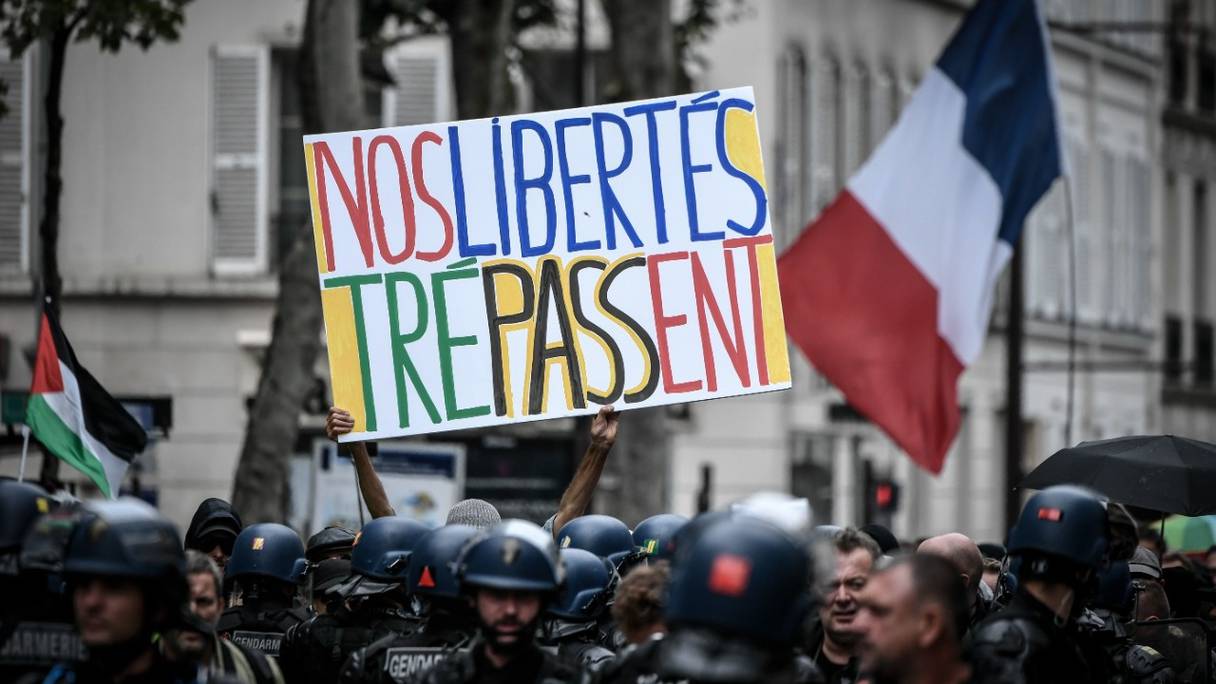 Un protestataire tient une pancarte devant des gendarmes lors d'une manifestation contre le pass sanitaire, qui permet d'accéder à la plupart des espaces publics, à Neuilly-sur-Seine, en région parisienne, le 7 août 2021.
