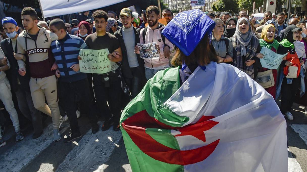 Une femme drapée dans un drapeau national algérien se tient devant des étudiants qui défilent lors d'une manifestation à Alger, le 16 mars 2021.
