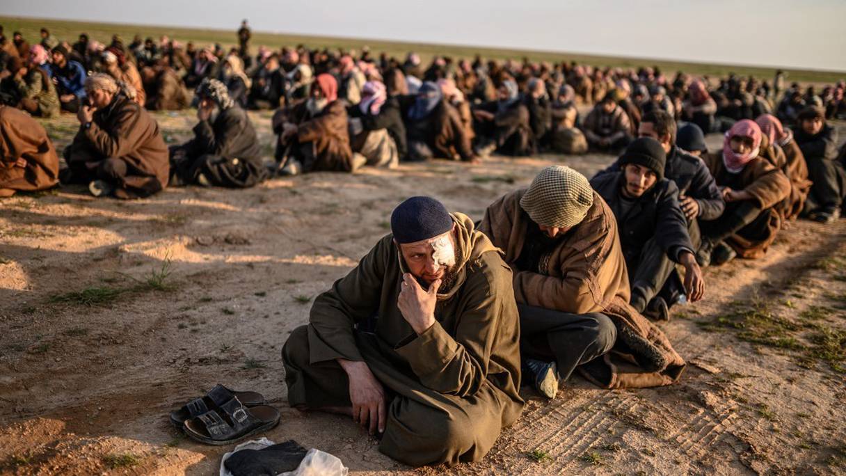 Des hommes soupçonnés d'être des combattants de l'Etat islamique (EI) attendent d'être fouillés par des membres des Forces démocratiques syriennes (FDS) dirigées par les Kurdes, à Baghouz, au nord de la Syrie (photo d'archive prise le 22 février 2019). 
