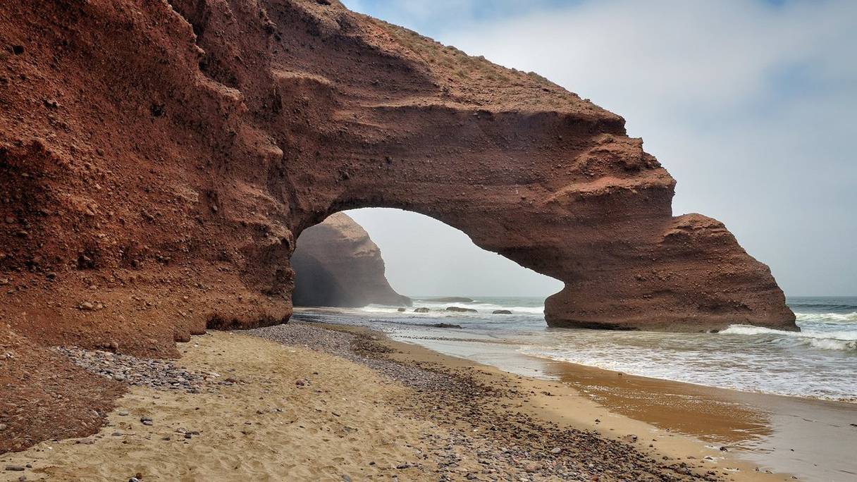 Plage de Legzira, à 10 km au nord de Sidi Ifni, au sud d'Agadir. En 2016, l'une de ses deux célèbres arches s'est écroulée, à cause de l'érosion. Dans cette région de l'Anti-Atlas, pêche, surf et sports extrêmes comme le parapente sont pratiqués.
