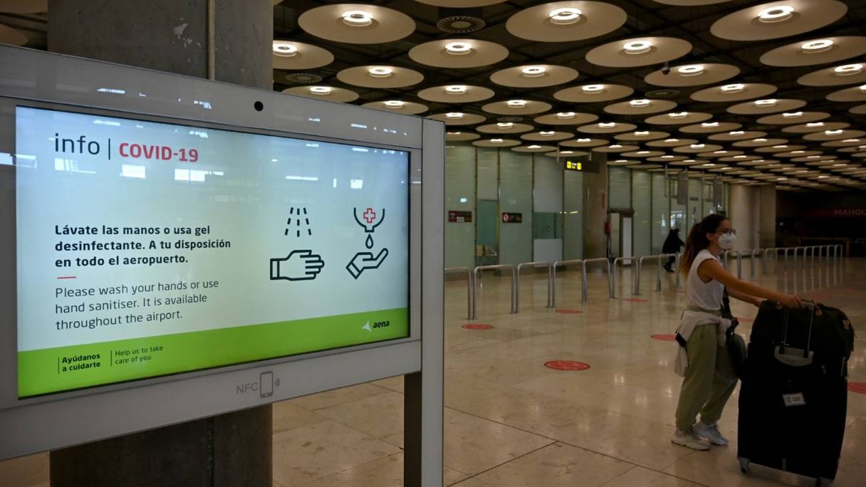 Une voyageuse passe devant une pancarte d'information Covid-19 au terminal 4 de l'aéroport Adolfo Suarez Barajas de Madrid, le 23 mars 2021.
