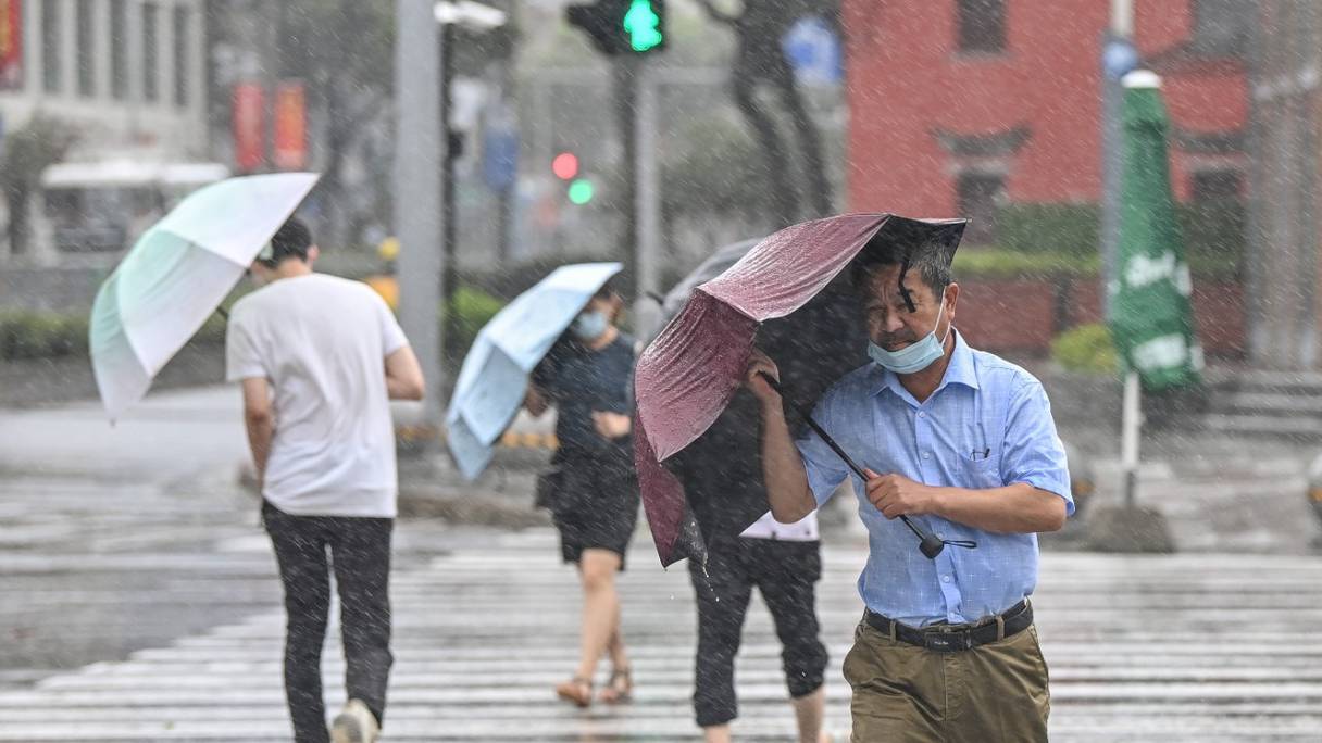 Des personnes traversent la rue dans le vent et la pluie à Ningbo, le 25 juillet 2021, alors que le typhon In-Fa frappe la côte est de la Chine.
