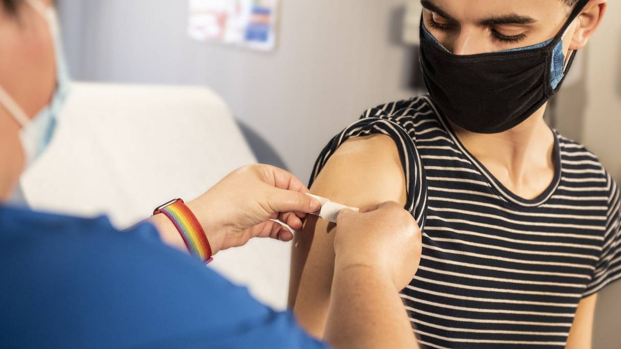 Une infirmière pose un pansement à un adolescent au point d'injection du vaccin.
