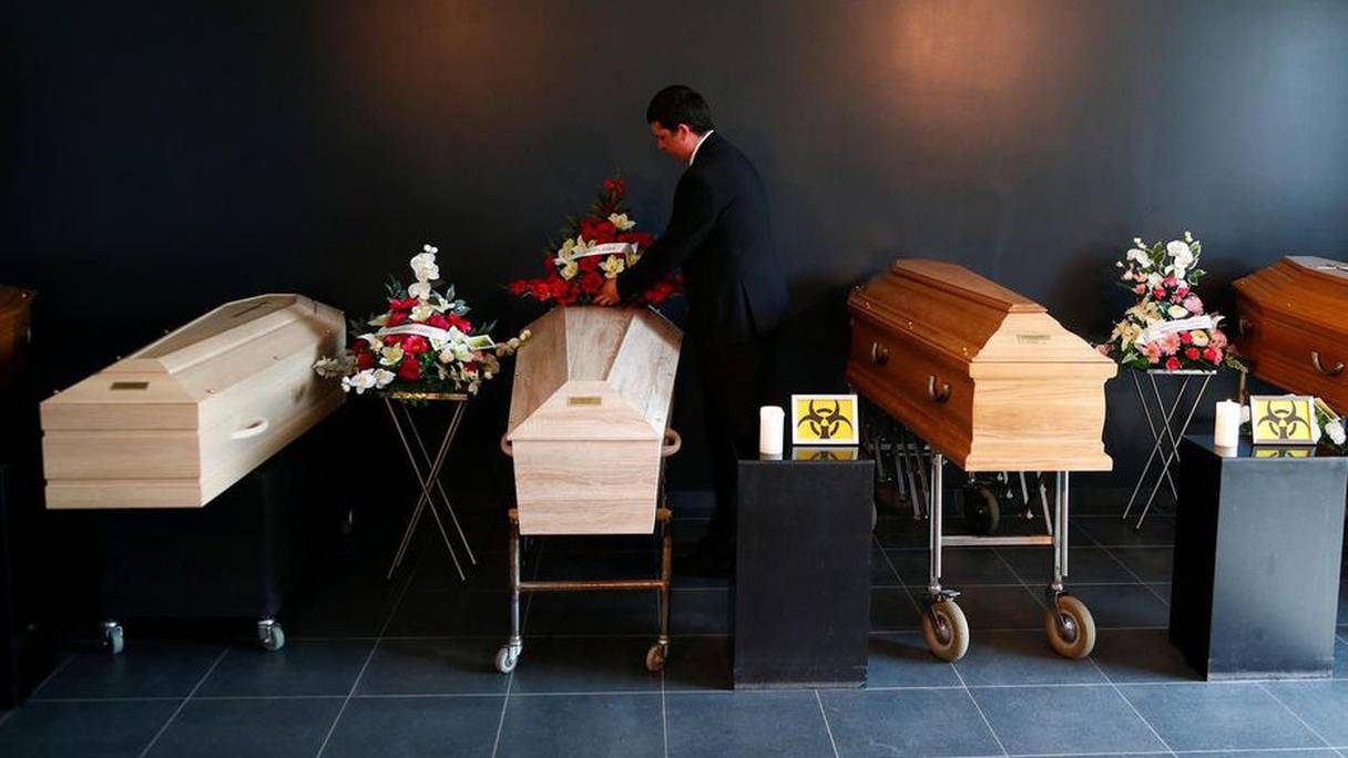 Un employé des pompes funèbres dépose des couronnes sur les cercueils en l'absence des familles.
