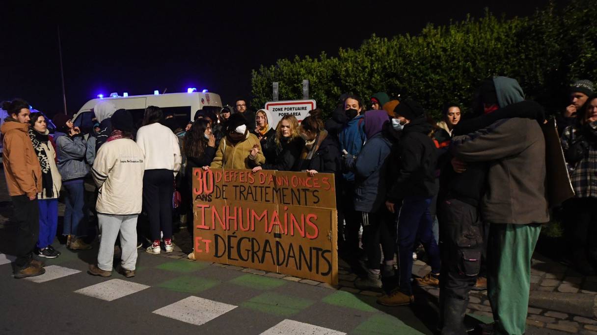 Des membres d'associations de défense des migrants, à côté d'une pancarte indiquant "30 ans d'annonces, de traitements inhumains et dégradants", le 24 novembre 2021 à Calais, dans le nord de la France, après le naufrage d'un bateau de migrants traversant la Manche.
