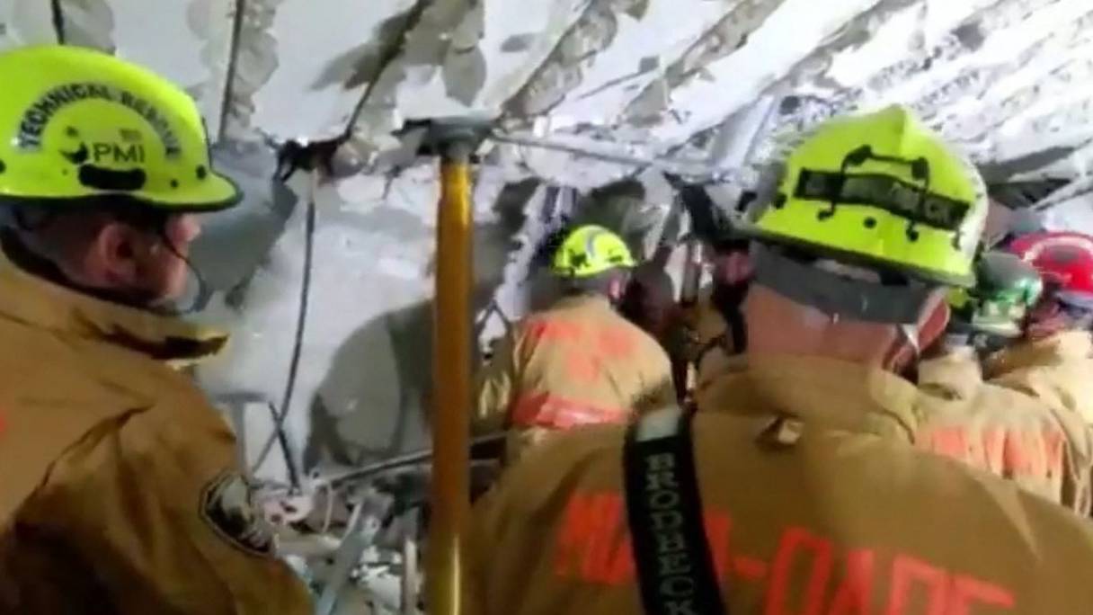 Cette capture d'écran extraite d'une vidéo publiée par le Miami-Dade Fire Rescue montre des pompiers travaillant dans le parking du sous-sol des tours Champlain après l'effondrement partiel du bâtiment à Surfside, au nord de Miami Beach, le 24 juin 2021. 
