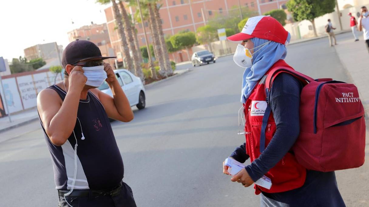 Une bénévole du Croissant-Rouge distribue un masque de protection à un passant, lors d'une opération de sensibilisation sur les conséquences du Covid-19, à Laâyoune, le 21 août 2021.
