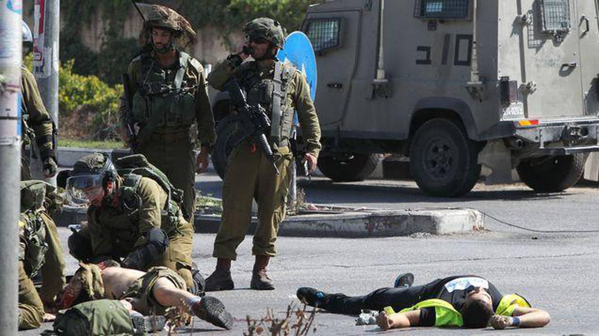 Des soldats israéliens portent secours à un des leurs (g) alors que le corps du palestinien auteur du coup de couteau gît au sol (d).
