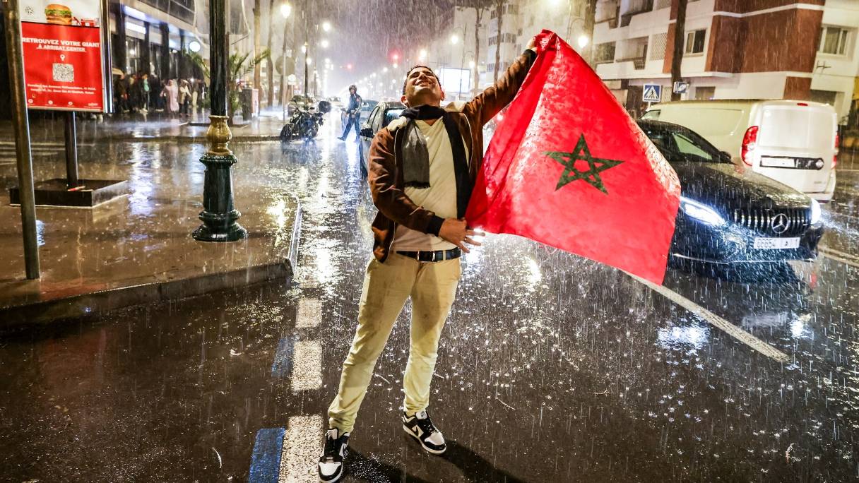 Un supporter marocain sous la pluie, tenant le drapeau national lors de la demi-finale de la Coupe du monde Qatar 2022 entre le Maroc et la France, à Rabat le 14 décembre 2022. 
