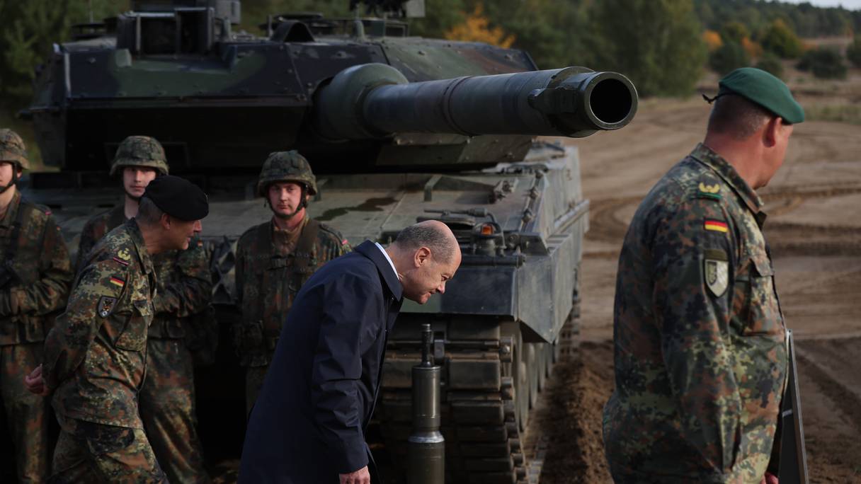 Photo d'archive prise le 17 octobre 2022 montrant le chancelier allemand Olaf Scholz (C) baissant la tête alors qu'il passe devant un char de combat Leopard 2 de la Bundeswehr.