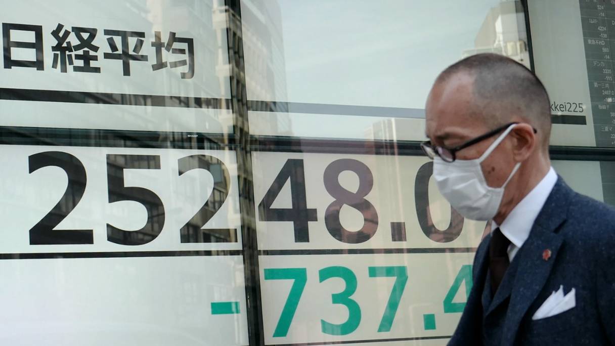 Un piéton passe devant un tableau indiquant le prix d'actions de la Bourse de Tokyo, au Japon, le 7 mars 2022.
