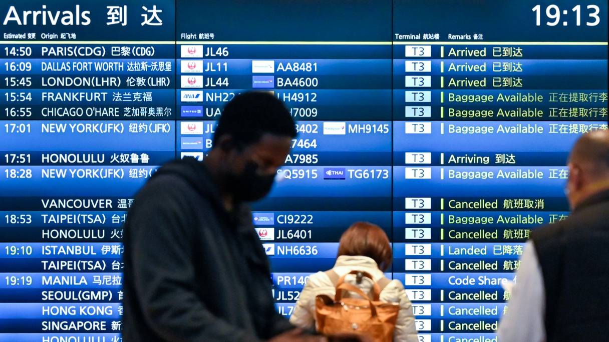 Des gens se tiennent devant le panneau des arrivées montrant des vols annulés à l'aéroport international Haneda de Tokyo, le 30 novembre 2021.
