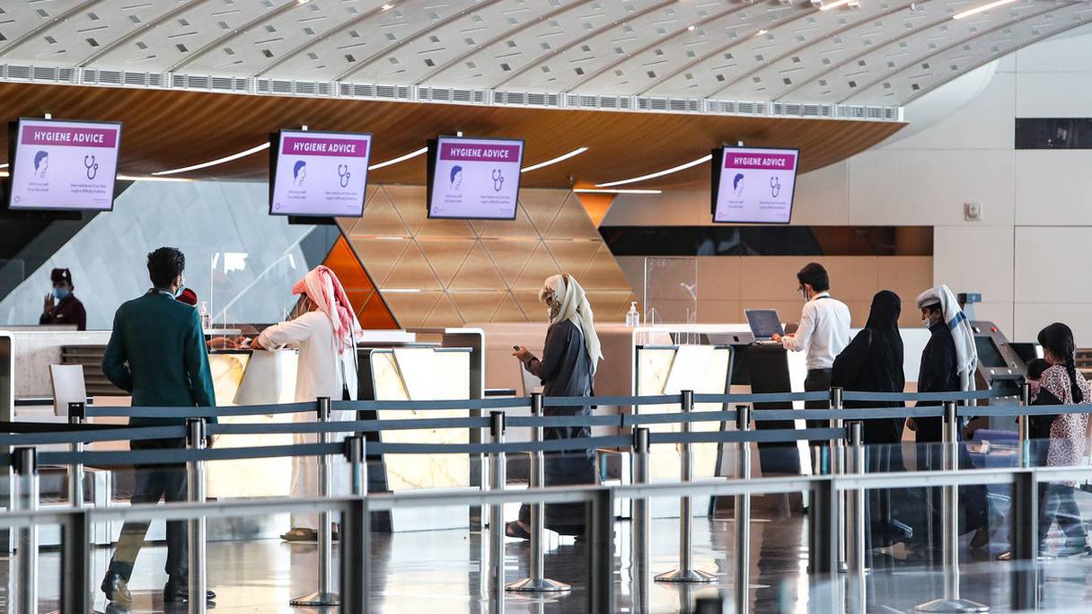 Des voyageurs masqués en raison de la pandémie de Covid-19, attendent au comptoir d'enregistrement de Qatar Airways, avant un vol à l'aéroport international Hamad, près de la capitale qatarie Doha, le 18 janvier 2021.
