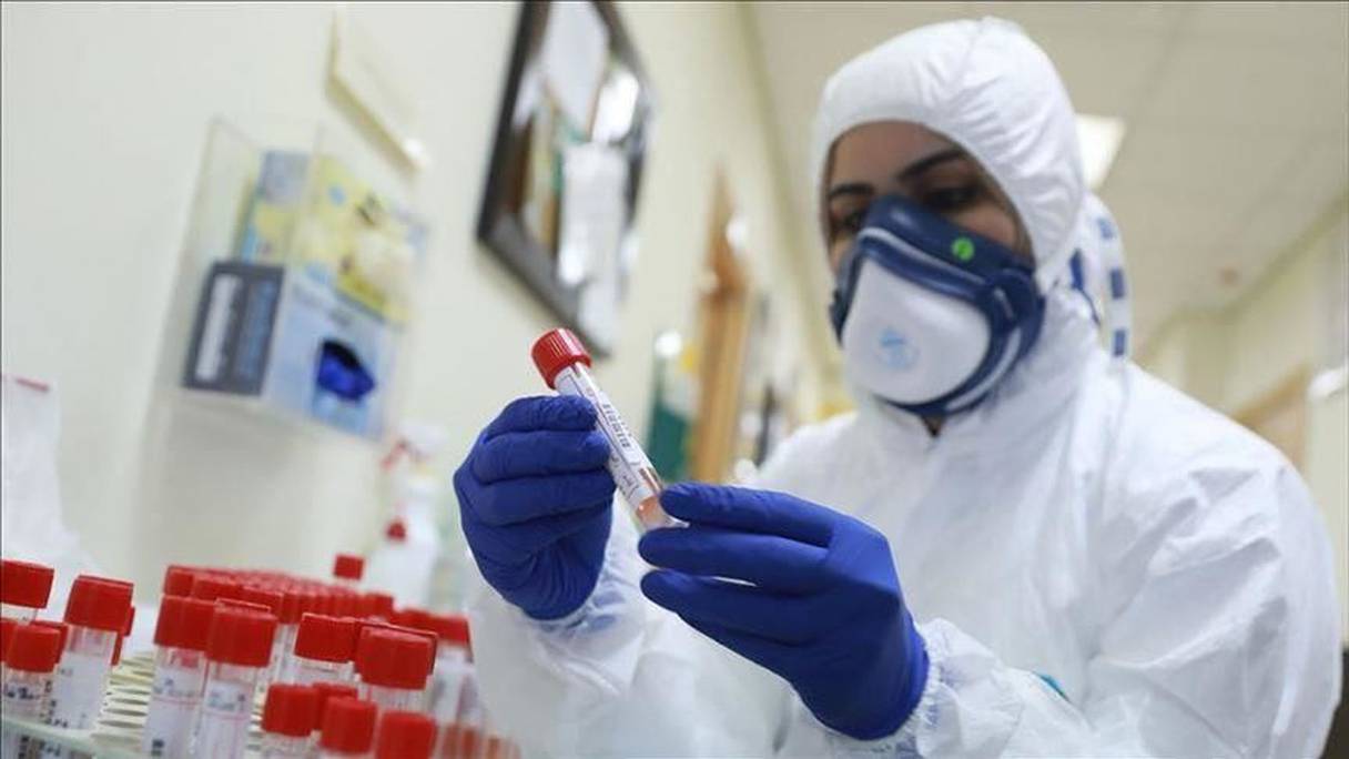 Prélèvements hermétiquement scellés dans un laboratoire d'analyses médicales, où une biologiste travaille en tenue de protection de rigueur. 
