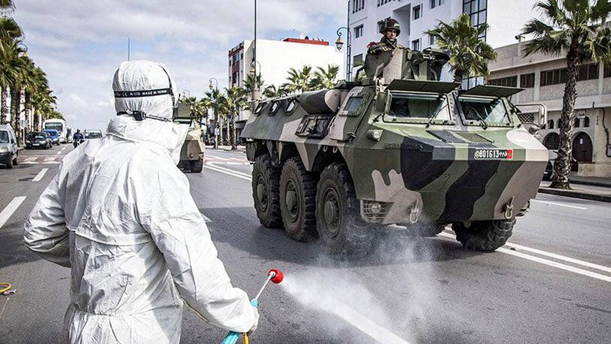 Des employés du ministère de la Santé désinfectent une rue pendant qu'un véhicule militaire blindé patrouille dans la capitale, Rabat, le 22 mars 2020.
