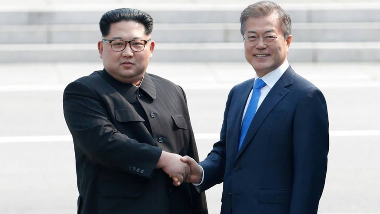 Moon Jae-in (d) et Kim Jong Un se serrent la main sur la ligne de démarcation avant le début du sommet, le 27 avril 2018 à Panmunjom.
