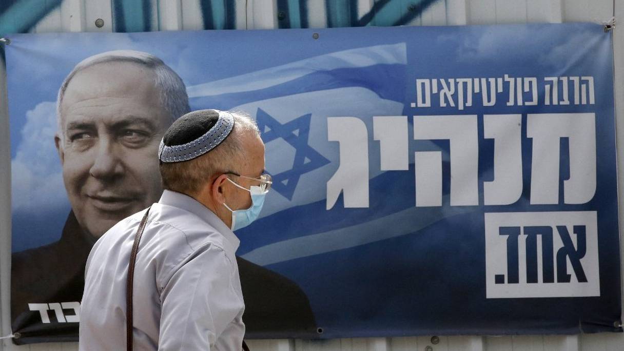 Un homme portant une kippa passe devant une bannière électorale du Likud israélien représentant le Premier ministre Benjamin Netanyahu. Une devise en hébreu mentionne: "de nombreux hommes politiques, un chef", à Beer Sheva, dans le sud d'Israël, le 22 mars 2021.
