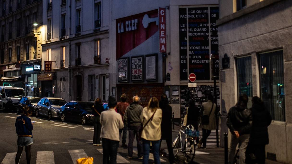 Des personnes se tiennent devant le cinéma d'arts et d'essai La Clef pour y regarder un film projeté sur la façade d'un immeuble, le 1er mai 2020 à Belleville, à Paris, au 46e jour d'un strict confinement en France pour faire cesser la propagation du Covid-19.
