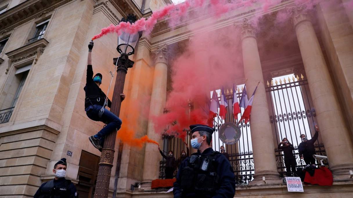 Des militants de l'organisation Extinction Rebellion (XR) tiennent une fusée fumigène, enchaînés aux portes de l'Assemblée nationale, à Paris le 4 mai 2021, lors d'une manifestation pour protester contre le projet de loi sur le climat. 
