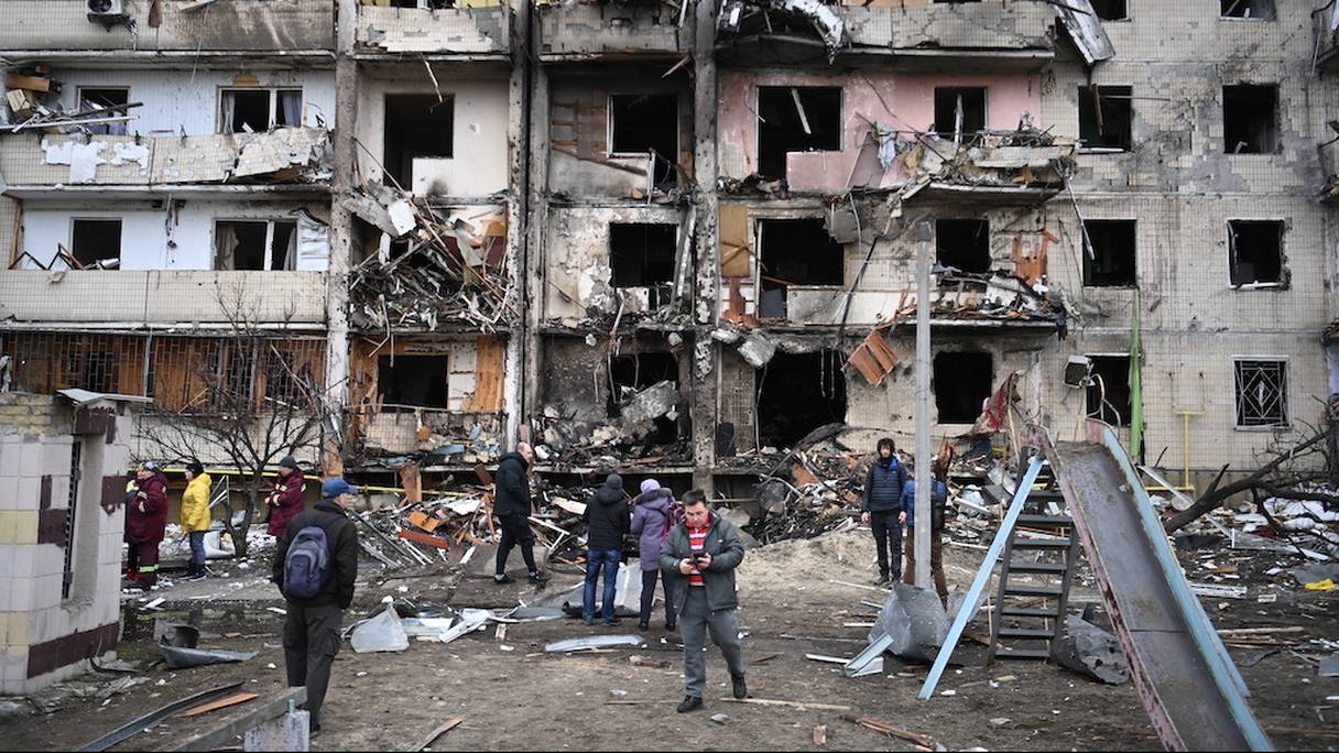 Les gens se rassemblent devant un immeuble résidentiel endommagé dans la rue Koshytsa, une banlieue de la capitale ukrainienne Kiev, le 25 février 2022.
