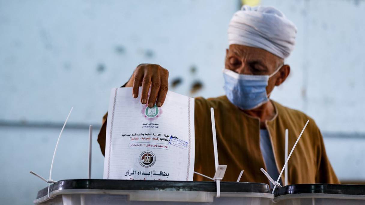 Un homme masqué glissant son bulletin dans l'urne dans un bureau de vote à Talibeya à Gizeh.
