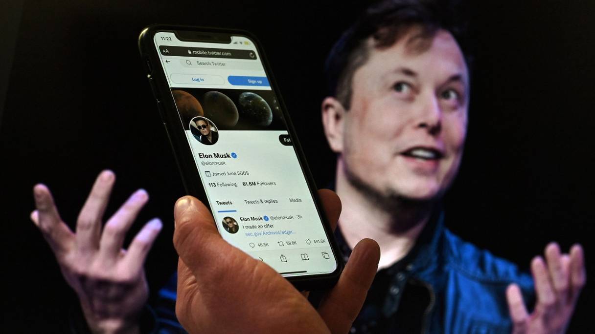 Compte Twitter d'Elon Musk sur un écran de téléphone, avec une photo de lui en arrière-plan. Le milliardaire a proposé de poursuivre son rachat du réseau social au prix initialement convenu, le 4 octobre 2022, pour 44 milliards de dollars.
