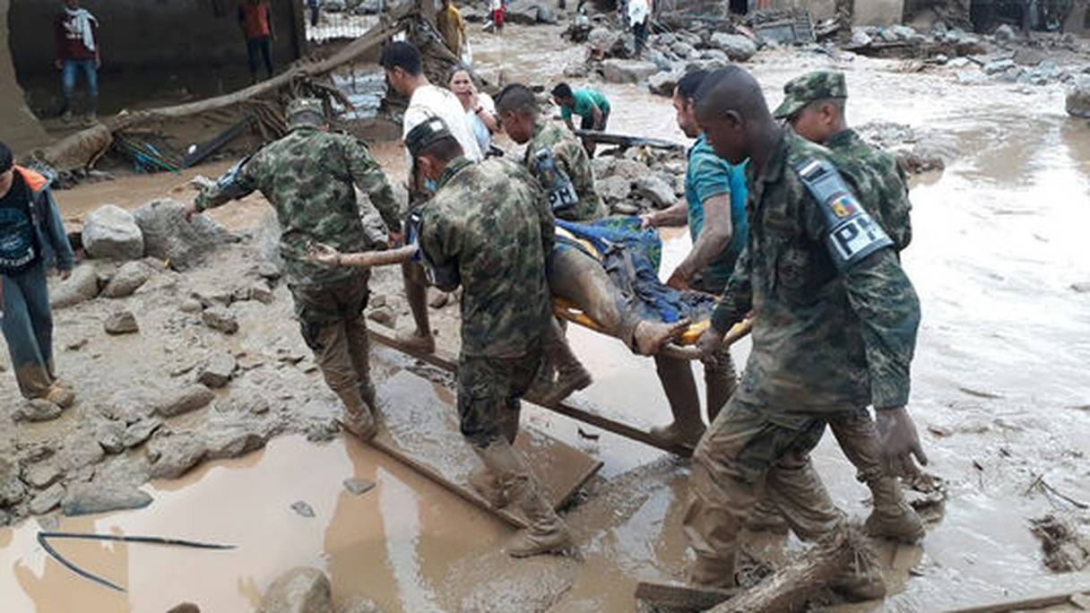 Pataugeant dans la boue, des secouristes apportent leur aide aux sinistrés.
